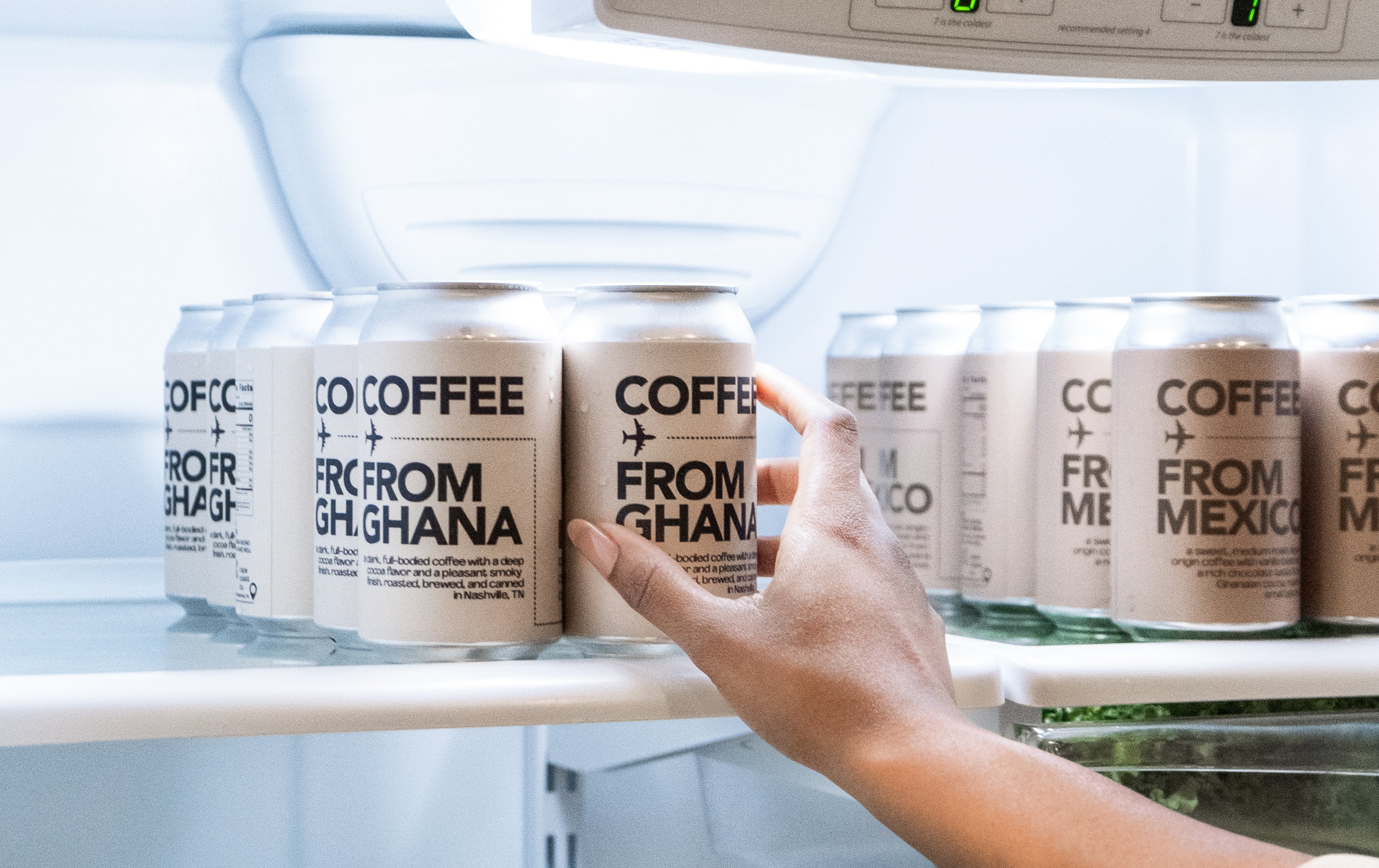 Hand reaching for a can of COFFEE FROM GHANA in a refrigerator.